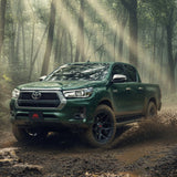 Green Toyota Hilux driving through a forest with sunlight filtering through the trees.