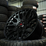 Black alloy wheel with a red logo on a stack of tires in a warehouse setting